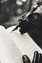 In this striking black and white image, gloved hands are writing in an open book with a feather pen, evoking a vintage and mysterious feel.